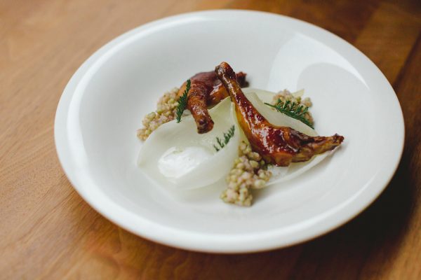 Cebolla tierna confitada, muslo de pichón y escabeche de flor de saúco.